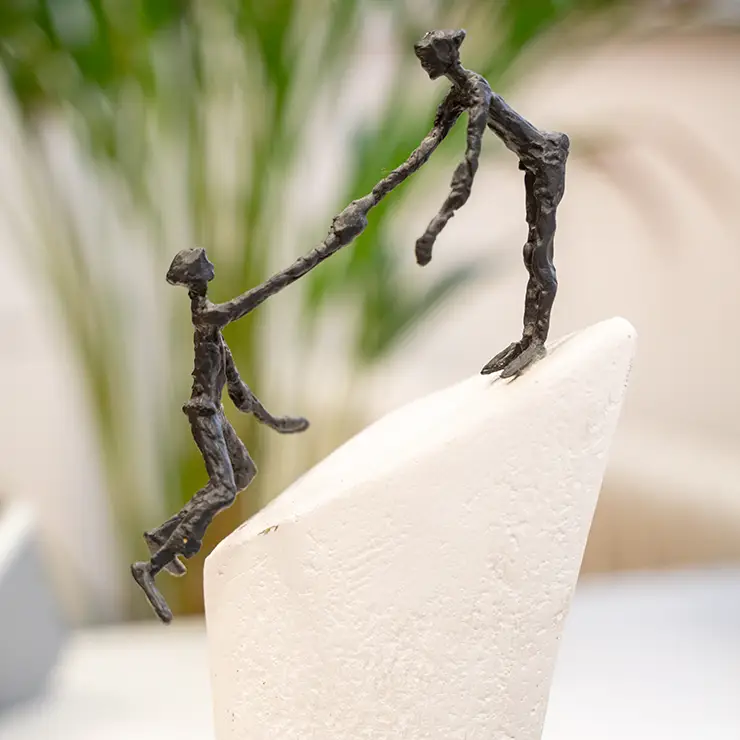 Zwei Figuren. Eine hilft der Anderen hoch.